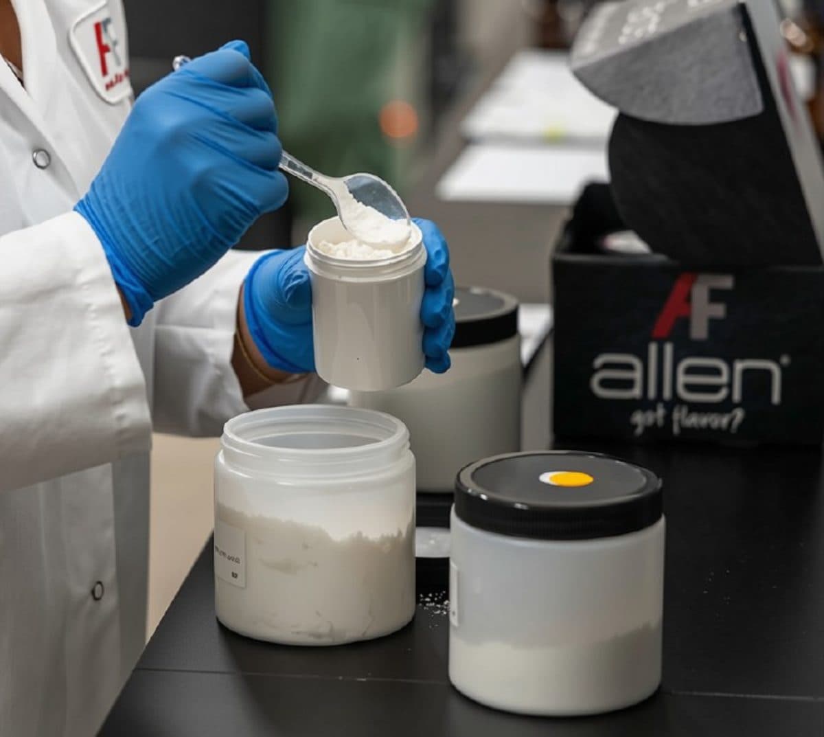 Technician scooping dry flavor powder into a jar at the Allen Flavors bench