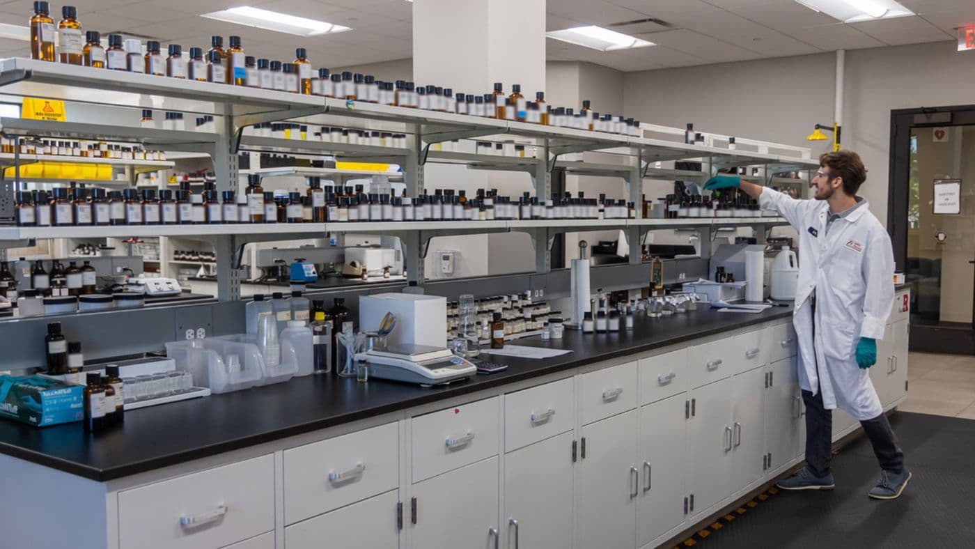 Allen Flavors library wall of labeled flavor bottles above the formulation bench