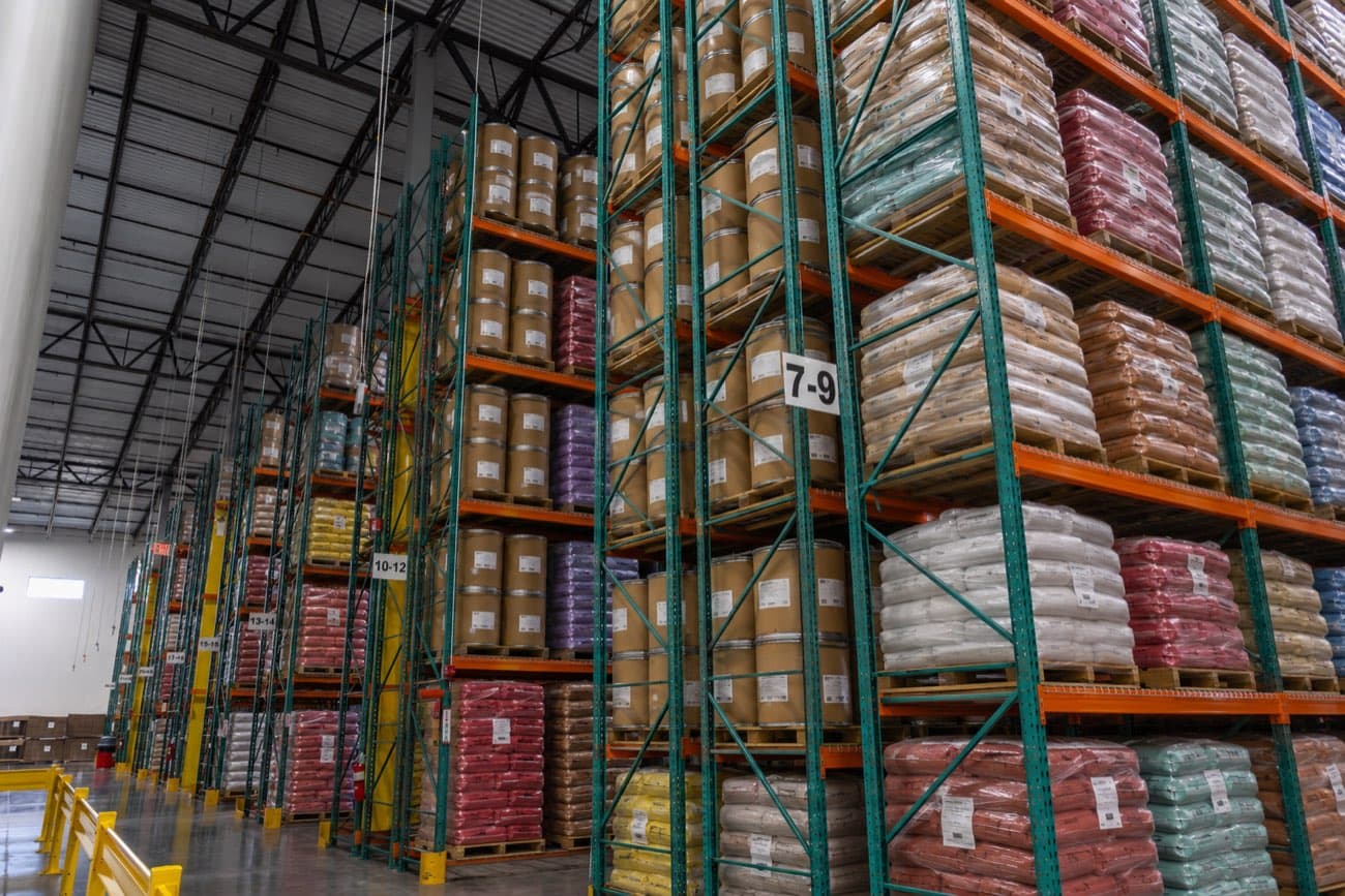 Racked warehouse aisle stacked with fiber drums and bagged ingredients